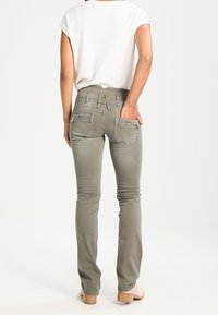Khaki skinny jeans med en mellem høj talje, to baglommer og detaljeret syning. Båret med en hvid kortærmet top.