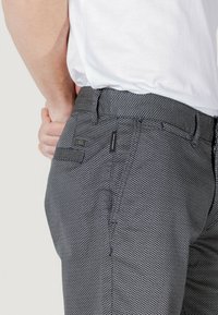 Pantaloni grigi a righe con un design strutturato, dotati di passanti per cintura e tasche laterali, indossati con una camicia bianca.