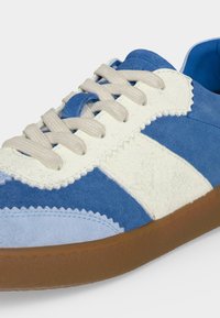 Μπλε και λευκό δερμάτινο αθλητικό παπούτσι με μπεζ κορδόνια και καφέ λαστιχένια σόλα, που δείχνει λεπτομερείς ραφές και υφές υλικών.