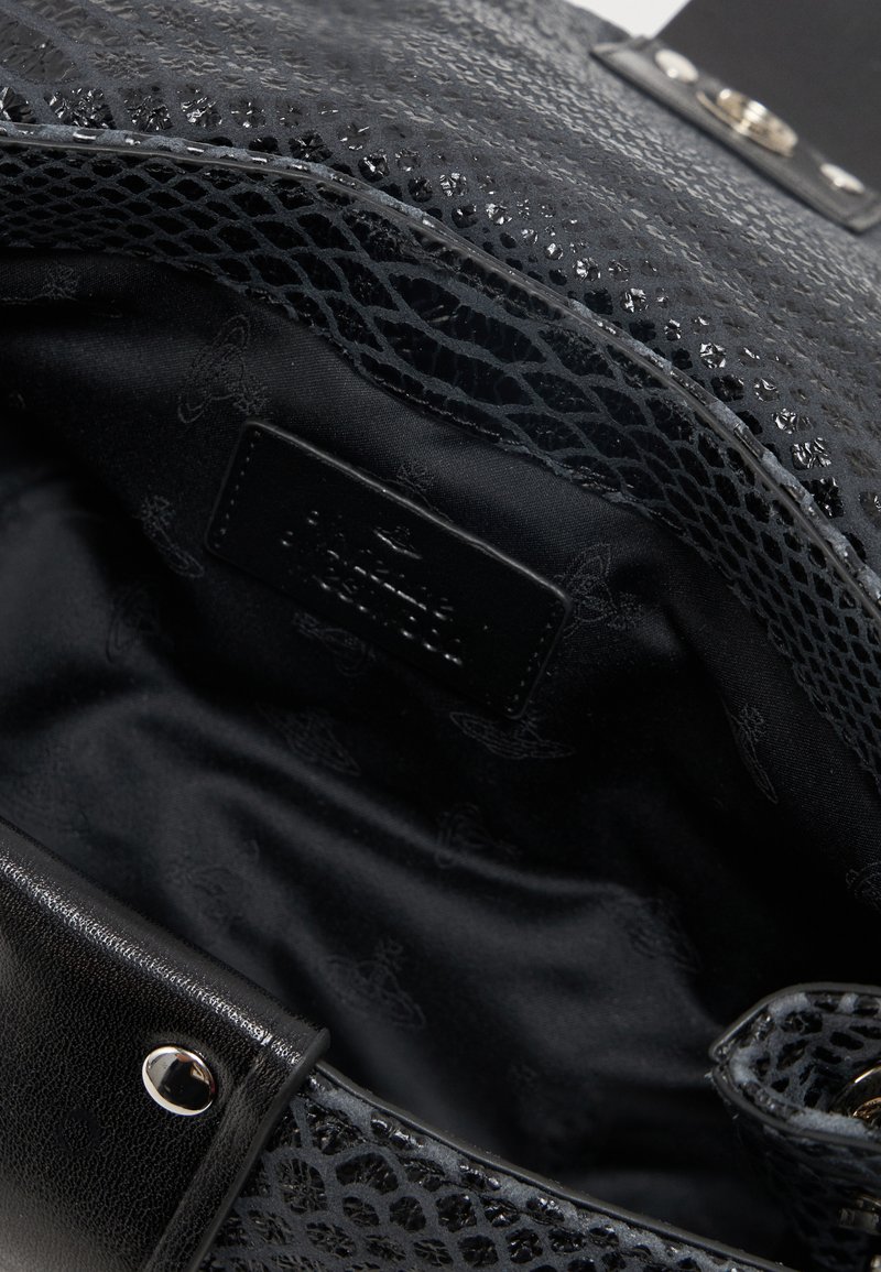 Intérieur d'un sac en cuir noir texturé avec une doublure en tissu noir à motif papillon et une lanière en cuir noir avec un bouton-pression argenté.