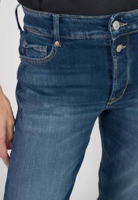 Blauwe denim jeans met een middelhoge taille, voorzien van vijf zakken, metalen knoopsluitingen en subtiele vervagingdetails op de benen.