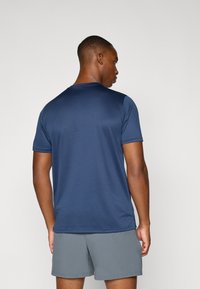 Dunkelblaues Kurzarmhemd mit Rundhalsausschnitt und seitlichen Schlitzen. Glatte Textur, minimalistisches Design, kombiniert mit grauen Shorts.