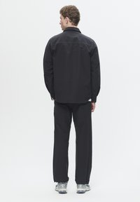 Black long-sleeve shirt with button cuffs, paired with loose-fitting black pants and silver athletic shoes, viewed from the back.