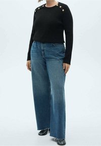 Pull en maille noire avec boutons aux épaules assorti à un jean large bleu taille haute. Texture lisse, coupe décontractée et ourlet en denim effiloché.