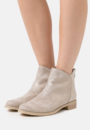 Bottines beiges à texture perforée, bout rond et petit talon bloc. Matière lisse et léger éclat soulignent le design.