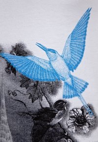 White T-shirt featuring a blue kingfisher illustration in flight, surrounded by black artistic elements and foliage details.