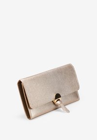 Diseño compacto de bolso de mano metálico beige, con una solapa redondeada y un cierre circular en tono dorado, sobre un fondo blanco.