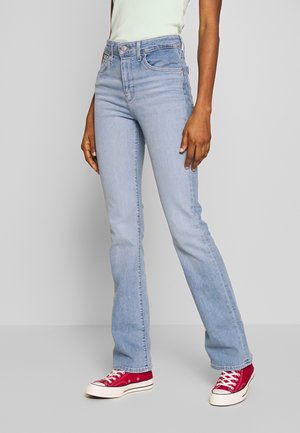 Person wearing light blue high-waist straight-leg jeans and red canvas sneakers, standing against a plain light gray background.