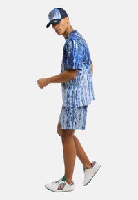 Blå mønstrete kortermet skjorte og shorts med virvlende design. Kombinert med en blå caps og hvite sneakers med fargeakenter.