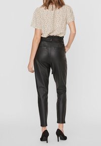Pantalons taille haute en simili cuir noir avec une coupe fuselée, assortis à un haut à manches courtes beige clair arborant un motif floral éparpillé.