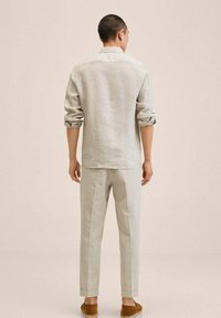Chemise en lin gris clair avec manches retroussées et col standard, associée à un pantalon de couleur claire et des sandales marron glissantes. Design minimaliste.