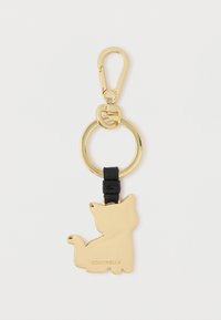 Kulta avaimenperä, jossa on kissan siluetti, kiinnitetty mustaan nahkahihnaan, jossa on kultainen kiinnitysklipsi helppoa kiinnittämistä varten.