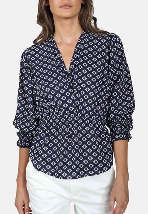 Marinebluse med hvid diamantmønster, samlede ærmer, v-hals-design og elastisk talje. Letvægtsstof med subtil tekstur.