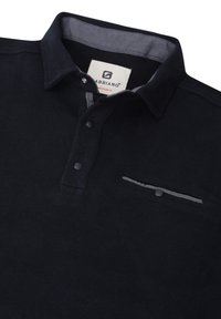 Polo nero con superficie testurizzata, colletto grigio a contrasto, patta con tre bottoni e piccola tasca frontale con rifinitura a contrasto.