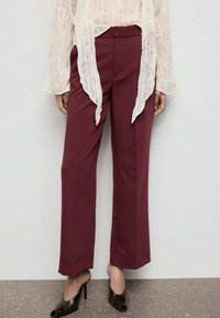Pantalones de pierna ancha burdeos con una textura suave, cintura alta y un corte ajustado. Llevados con una blusa semitranslúcida de color claro y tacones.
