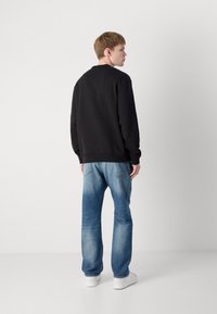 Black sweatshirt with ribbed cuffs, paired with light blue distressed jeans and white sneakers, viewed from the back.