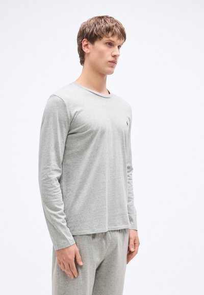 Šedé tričko s dlouhým rukávem z měkkého materiálu, s kulatým výstřihem a malým logem na hrudi. Nošeno s odpovídajícími šedými kalhotami.