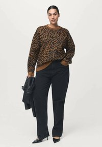 Jersey de leopardo en tonos marrón y negro, con cuello redondo y puños acanalados. Llevado con jeans negros rectos y sosteniendo una chaqueta negra.