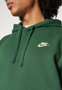 Person som bär en mörkgrön Nike-hoodie med dragsnören, synlig nacke, läppar och lockigt hår i en närbild.
