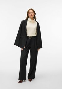 Czarna dopasowana marynarka na kremowym golfie, zestawiona z czarnymi spodniami z wysokim stanem i burgundowymi szpilkami na spiczastym nosku. Gładki materiał, luźny krój.