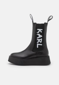 Black platform ankle boot with a smooth leather finish, elastic side panels featuring "KARL" in white, and pull tabs for easy wear.