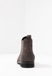 Brown suede ankle boot with a smooth texture, rounded toe, elastic side panels, and a low black heel. Back tab for easy wear.