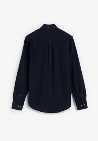 Camisa de manga larga azul marino con cuello de botones, detalle de pliegue trasero y puños abotonados; textura de tela suave.