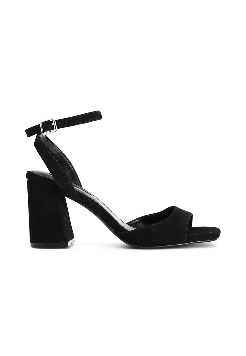 Sandalias de tacón alto de ante negro con tacón bloque, punta abierta y correa de tobillo ajustable. Textura suave y diseño minimalista.