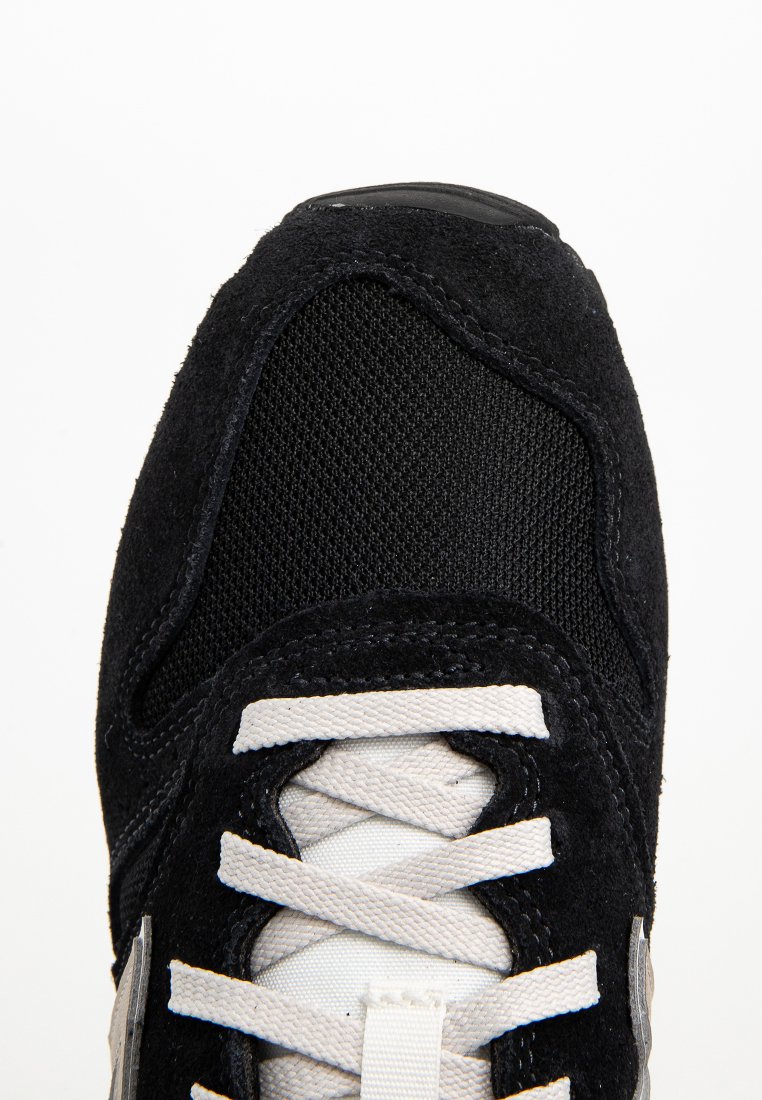 Nahaufnahme der schwarzen Sneaker-Zehen mit weißen Schnürsenkeln sowie Details aus Wildleder und Mesh unter hellem Licht.