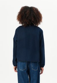 Marineblauwe jacket met een losse pasvorm, elastische mouwen en een ronde halslijn. Draag het met hoge taille blauwe denim jeans.