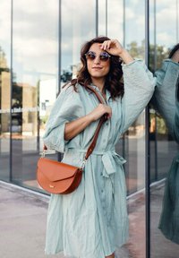 Světlé zelené texturované šaty button-up s páskem v pase, doplněné hnědou křížovou taškou se stříbrnými detaily a zakřiveným designem.