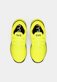 Gele sportschoenen met een bovenwerk van mesh, ronde veters en een zwarte buitenzool. De binnenzool heeft een logo en het modelnummer "CXT-2" zichtbaar.