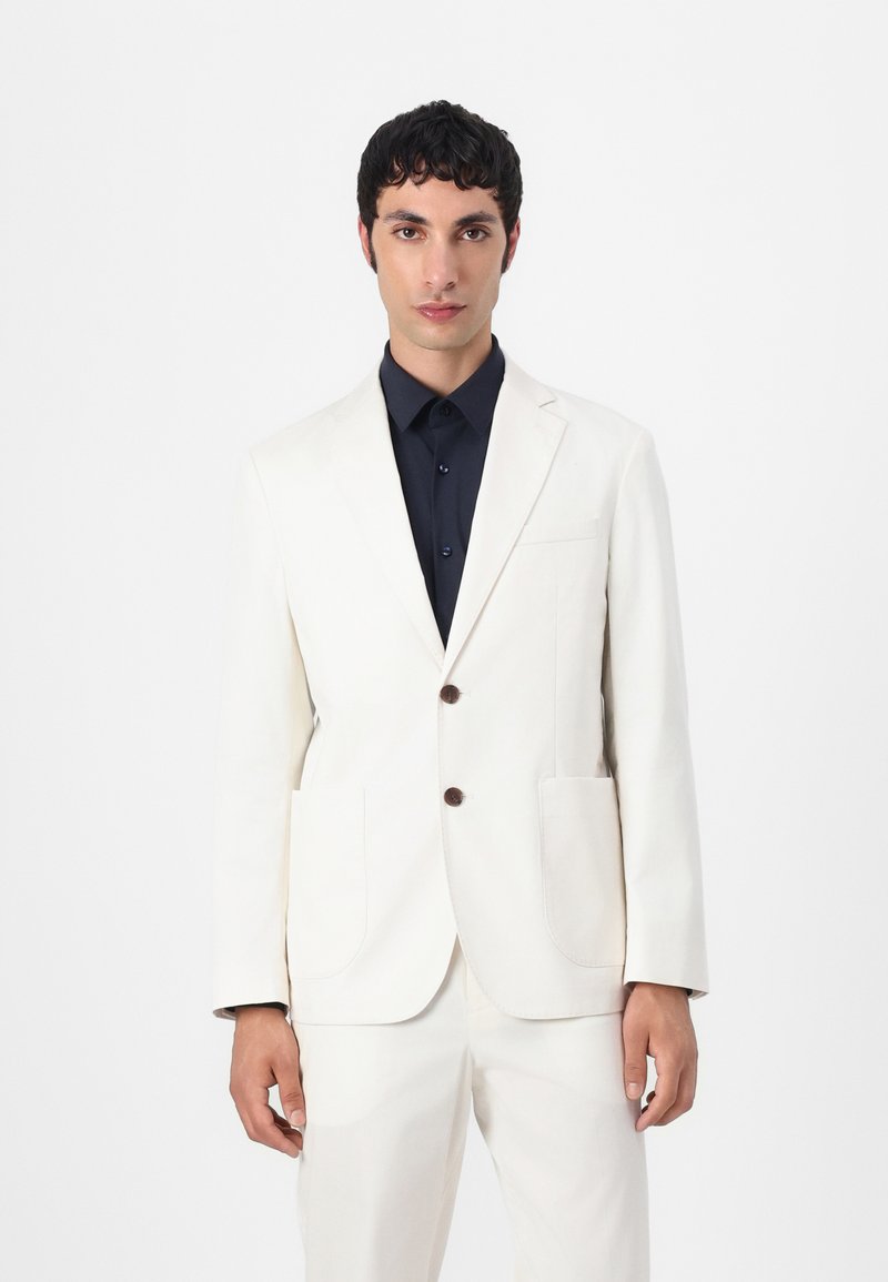 Witte katoenen blazer met notch kleppen, twee voorzakken en bruine knopen, gecombineerd met een donkerblauwe overhemdd. Slim fit ontwerp.