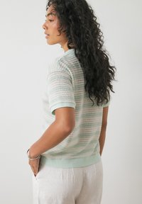 Pleteni pulover s kratkimi rokavi v mehkih mint in belih črtah. Strukturalna tkanina z udobnim krojem, ki vključuje rebrast ovratnik in manšete.