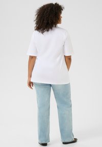 T-shirt blanc à manches courtes avec une coupe décontractée, associé à un jean droit bleu clair. Design simple, texture lisse et sans motifs visibles.
