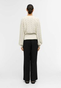 Suéter de punto crema con textura geométrica, dobladillo acanalado y mangas abullonadas, combinado con pantalones negros de pierna ancha.