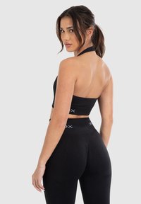 Zwarte sport-bh en hoge taille legging gemaakt van rekbare stof. De bh heeft een halternekontwerp; de tailleband heeft een logo-detail.