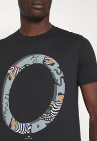 Schwarzes Baumwoll-T-Shirt mit einem zentralen Grafikdesign, das Zebras und farbenfrohe Akzente in einem kreisförmigen Muster zeigt, sowie einem Textüberlagerung.