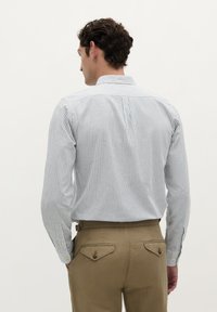 Camicetta a righe con bottoni in blu chiaro e bianco, in tessuto di cotone. Vestibilità tailored con yoke sulla schiena e colletto. Abbinata a chinos beige.