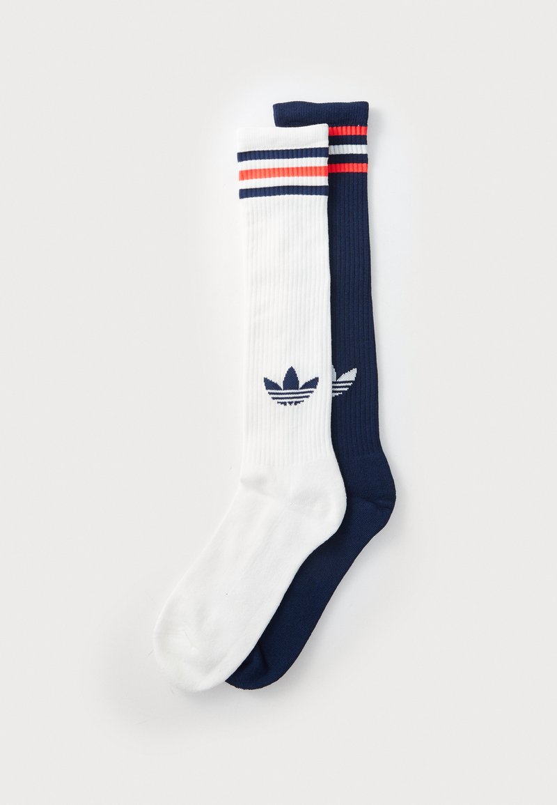 Bavlnené športové ponožky v bielej a námorníckej modrej farbe s ribovanou textúrou, so strapcami v červenej a modrej farbe a logom trefoil Adidas.
