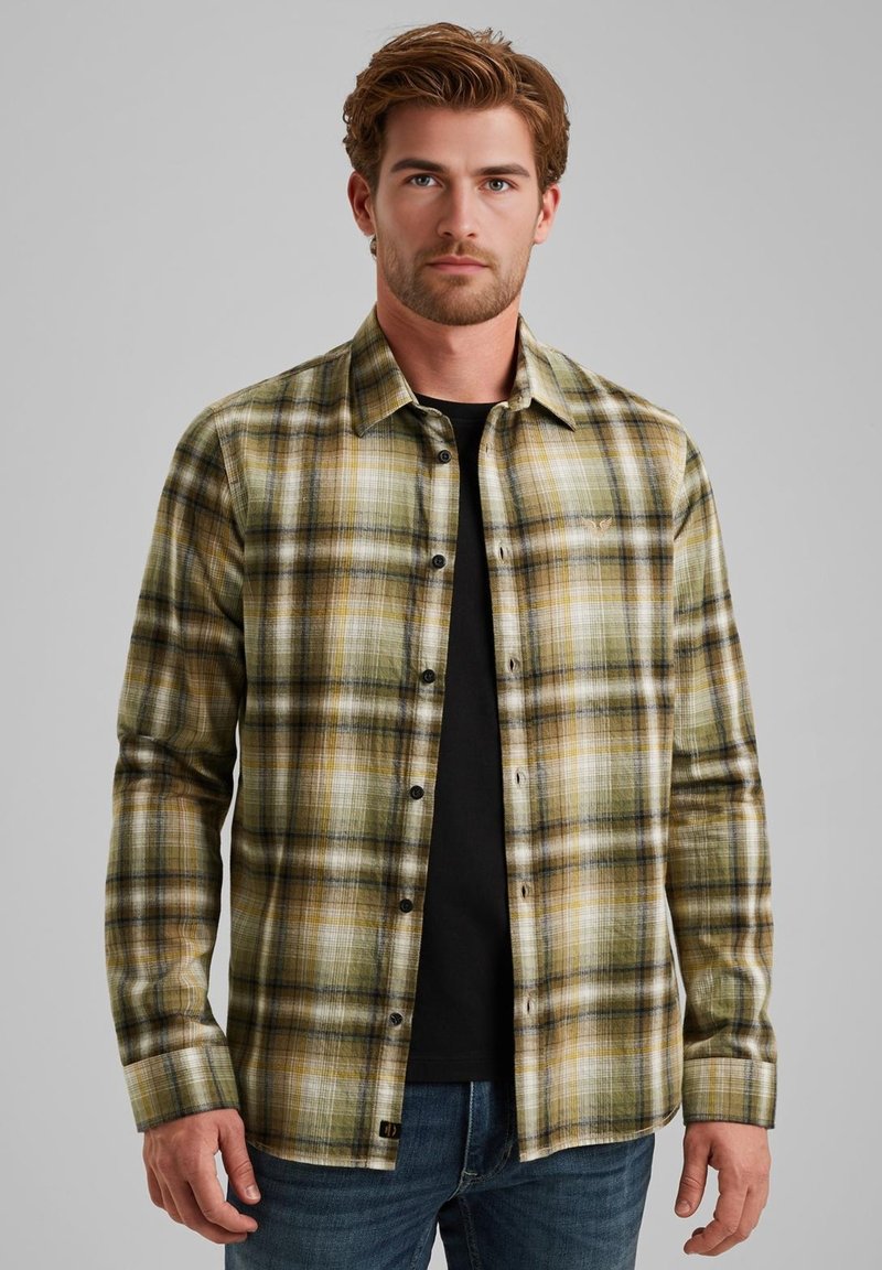 Camicia di flanella a quadri in tonalità verdi, gialle e nere; design con bottoni; maniche lunghe; indossata su una t-shirt nera; con cuciture visibili.