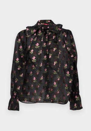 Blouse noire transparente avec un motif floral rose et vert, dotée d'un col à nœud papillon, d'une fermeture à boutons à l'avant et de manches longues avec des poignets froncés.