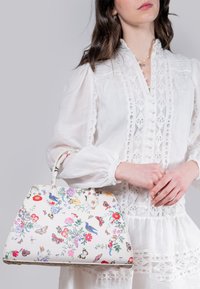 White handbag with floral and butterfly prints; smooth material; structured shape; dual handles and decorative stitching accents.