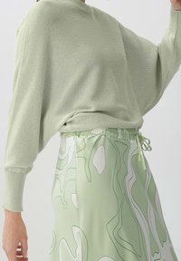 Hellegrüner, locker gestrickter Pullover mit weitengeschnittenen Ärmeln, kombiniert mit einem passenden Rock, der abstrakte weiße und grüne Muster sowie einen elastischen Bund aufweist.