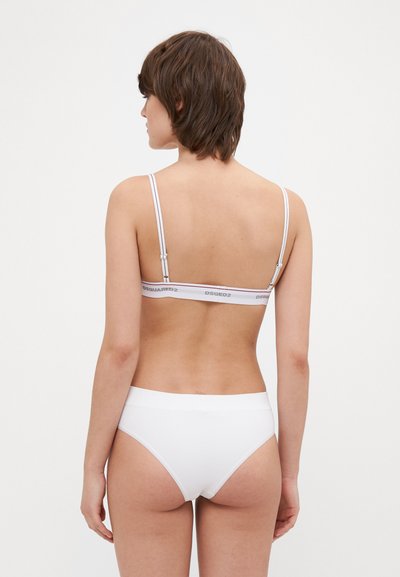Hvid bralette med justerbare stropper og logo-bånd, parret med hvide højhalsede trusser. Glat tekstur og minimalistisk design.