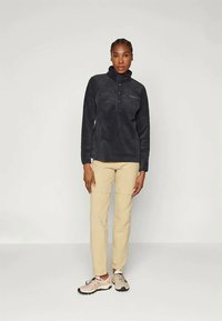 Fekete szőtt pulóver magas gallérral és gombos kivágással. Bézs nadrággal és világos színű sportcipővel párosítva. Egyszerű dizájn.