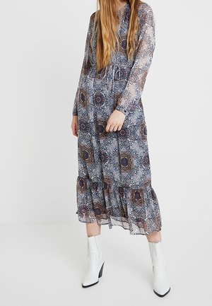 Lang, gennemsigtig kjole med et blomstermønster i marineblå, hvid og rustfarver. Den har bindebånd i taljen, lange ærmer og en flæsekant.