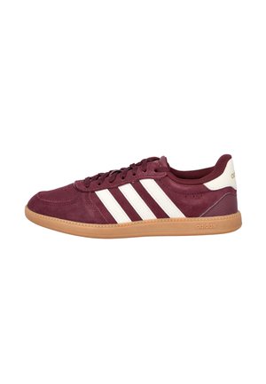 Zapatilla Adidas de corte bajo color granate con rayas blancas, suela de goma y lengüeta blanca en el talón sobre fondo blanco.