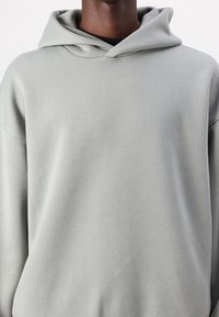 Lysegrå hættetrøje lavet af blødt stof med en afslappet pasform, der har snøre i hætten og lange ærmer.