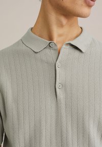 Cămașă polo texturată de culoare gri deschis, cu guler, având un model geometric și trei nasturi gri pe placket.